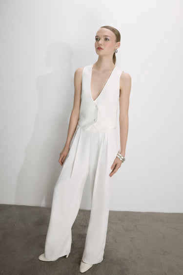 Model wearing a white sleeveless jumpsuit against a plain background