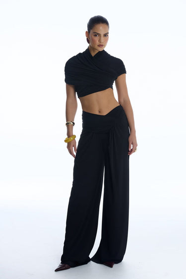 Woman wearing a black outfit with a cowl neck top and wide-leg pants on a white background