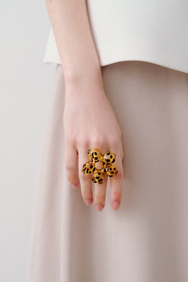 Hand wearing a leopard print ring on a plain background