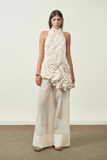 Woman wearing a white halter top and wide-leg pants against a plain background