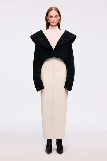 Woman wearing a black top with ruffled details and a beige skirt on a white background