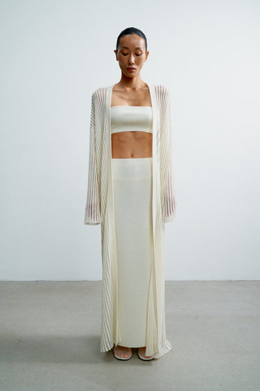 Woman wearing a white outfit with a sheer cover-up against a plain background