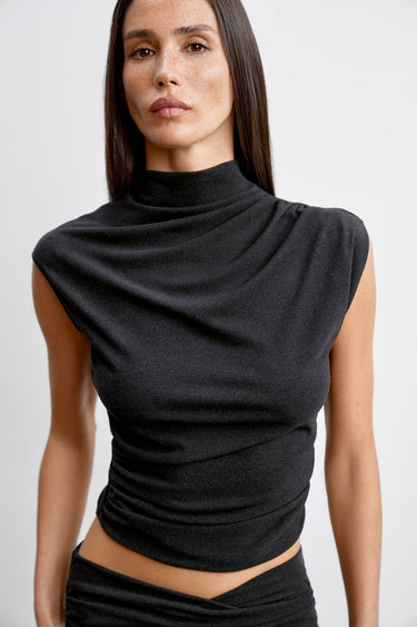 Woman wearing a black sleeveless top with a draped neckline against a white background