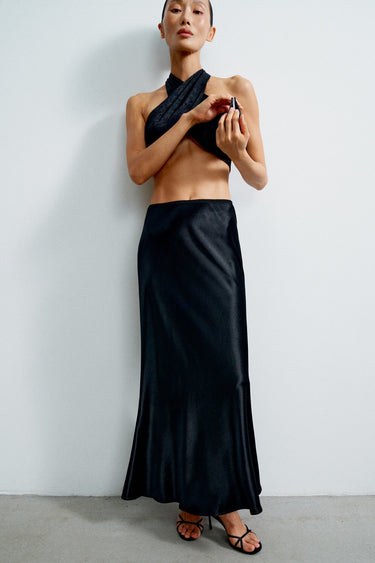 Woman wearing a black one-shoulder top and long skirt against a white background