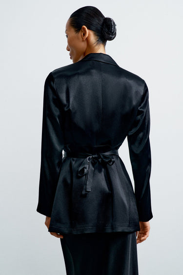 Person wearing a black satin jacket on a plain background