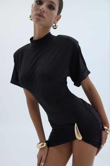 Woman wearing a black outfit with gold accents on a light gray background