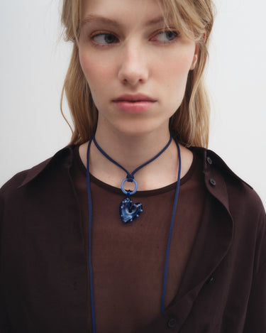 Person wearing a blue necklace with a circular pendant on a plain background