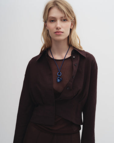 Woman wearing a brown shirt and blue necklace against a white background