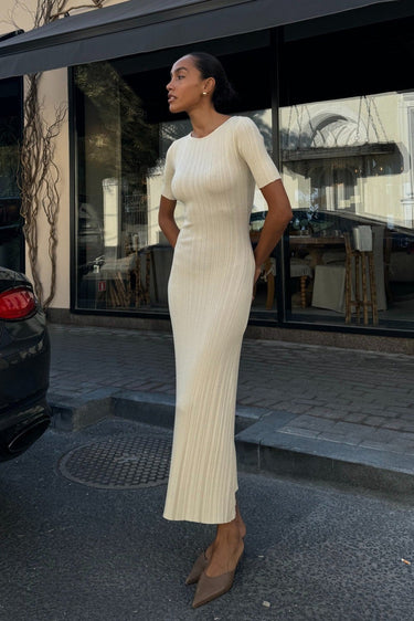Woman in a white dress standing outside a building with a glass door.