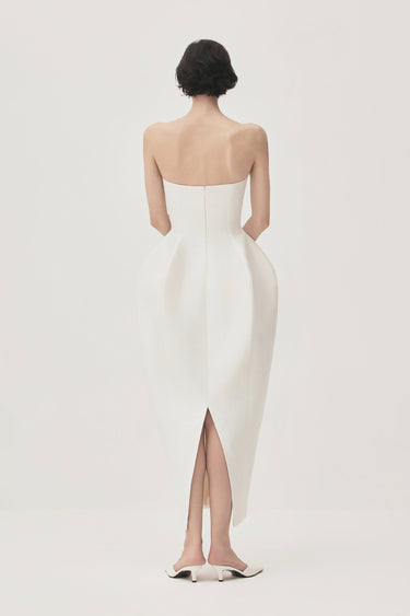 Woman wearing a strapless white gown with a slit on a plain background