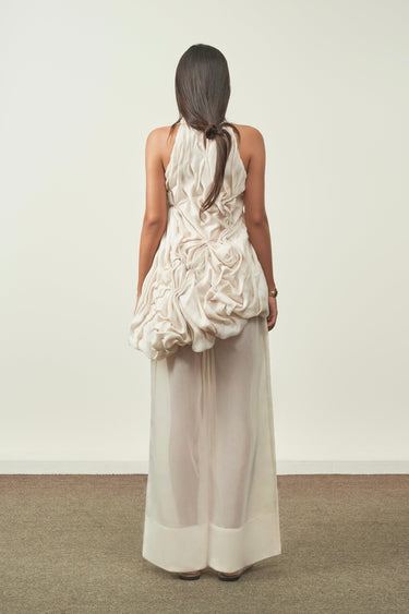 Woman wearing a white floral dress with sheer white pants against a plain background