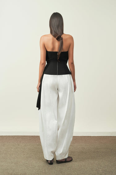 Woman wearing a black top and white pants against a plain background