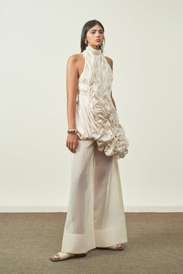 Woman wearing a white dress with ruffled top and wide-leg pants against a plain background