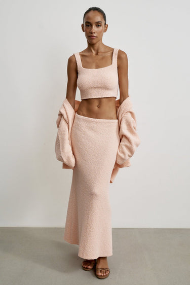 Woman wearing a pink outfit with a matching coat against a plain background