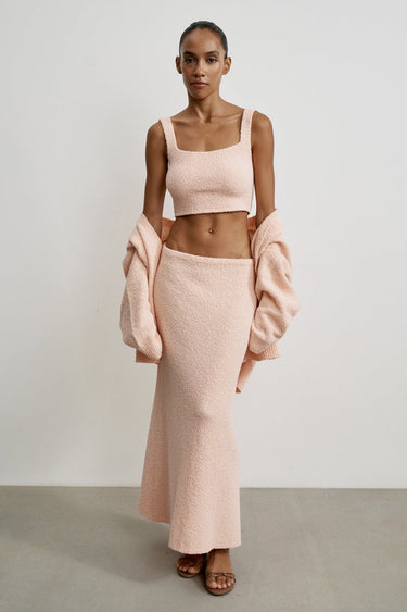 Woman wearing a pink outfit with a matching coat against a plain background