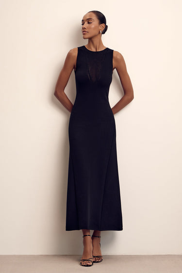 Woman wearing a black sleeveless dress against a plain background